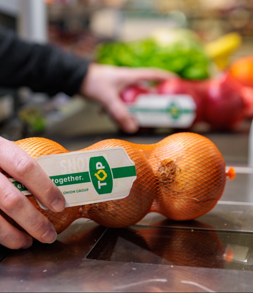 Gele uien in netje met label van TOP wordt afgerekend bij de kassa in de supermarkt van TOP The Onion Group