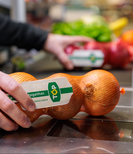 Gele uien in netje met label van TOP wordt afgerekend bij de kassa in de supermarkt van TOP The Onion Group